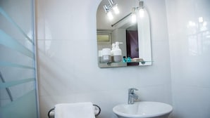 A bathroom with a white sink, a glass shower enclosure, and a mirror with toiletries. - Residence Maeva (Mamoudzou)