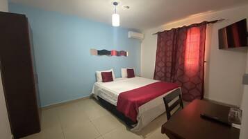 A room with a bed, a desk, a chair, a TV, and an air conditioning unit.