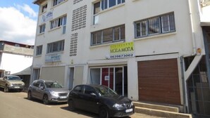 A multi-story building with a restaurant named 'MORA MORA' on the ground floor. There are several parked cars in front, and the building has multiple windows and balconies. - Residence Maeva (Mamoudzou)