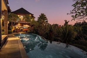 A poolside area with a wooden deck, lounge chairs, and umbrellas. - Yanyan Resort Ubud (Sukawati)