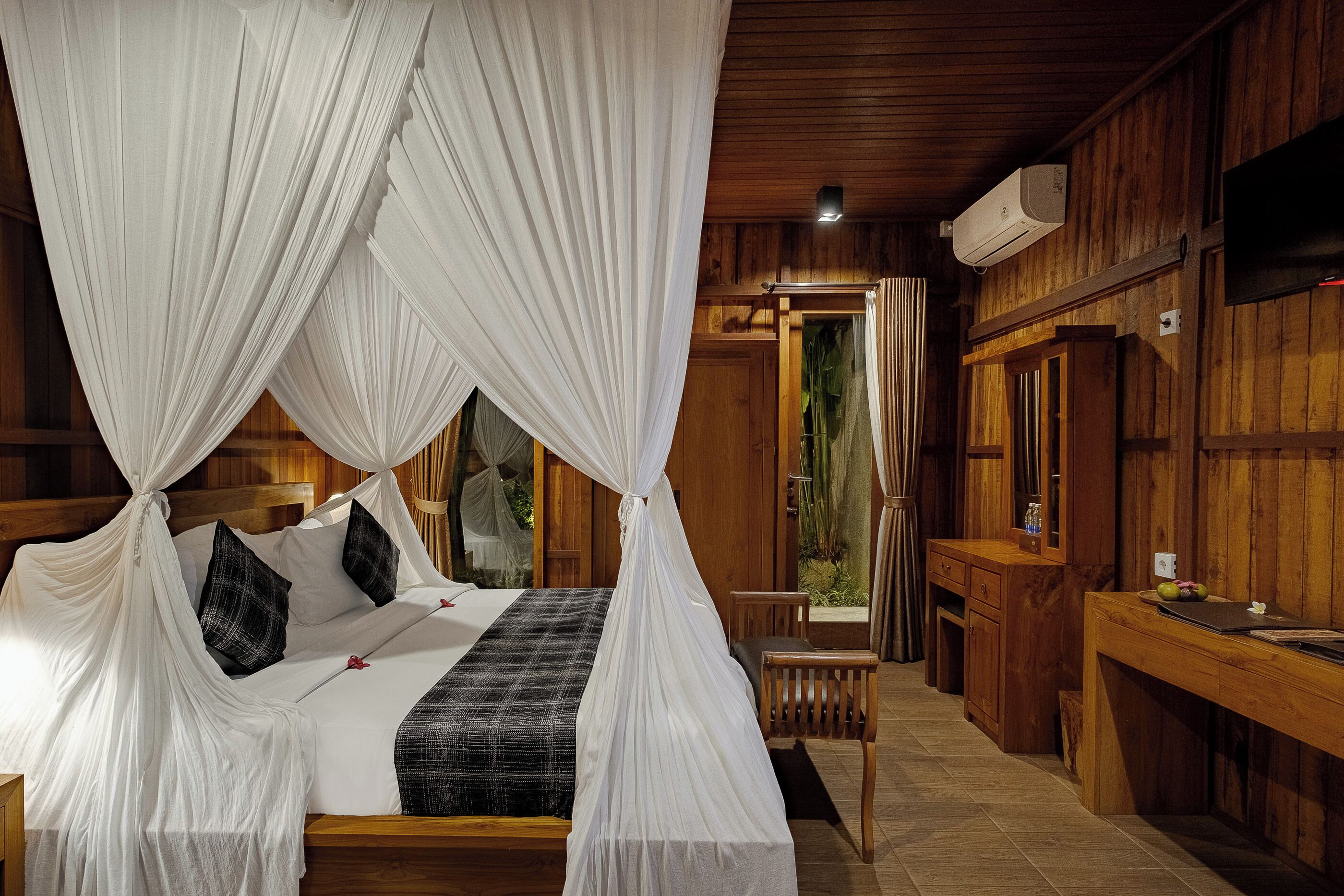 A bedroom with a canopy bed, wooden walls, a TV, and a small desk.