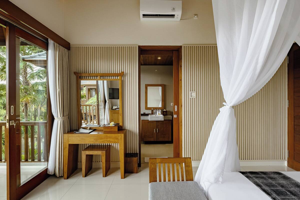 A room with a wooden desk, a bed, and a bathroom visible through an open door.