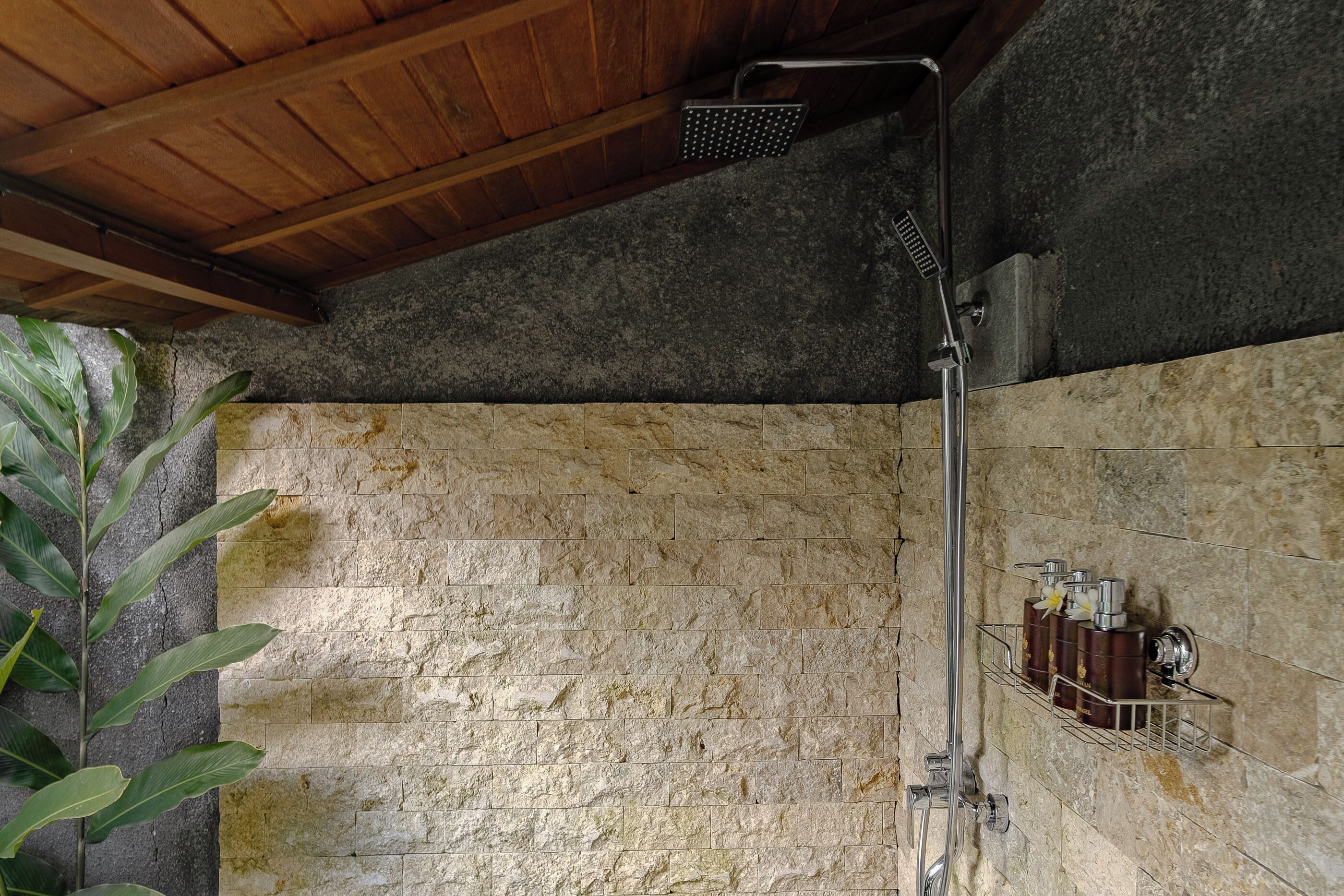 A shower area with a stone wall, a wooden ceiling, and a metal showerhead.