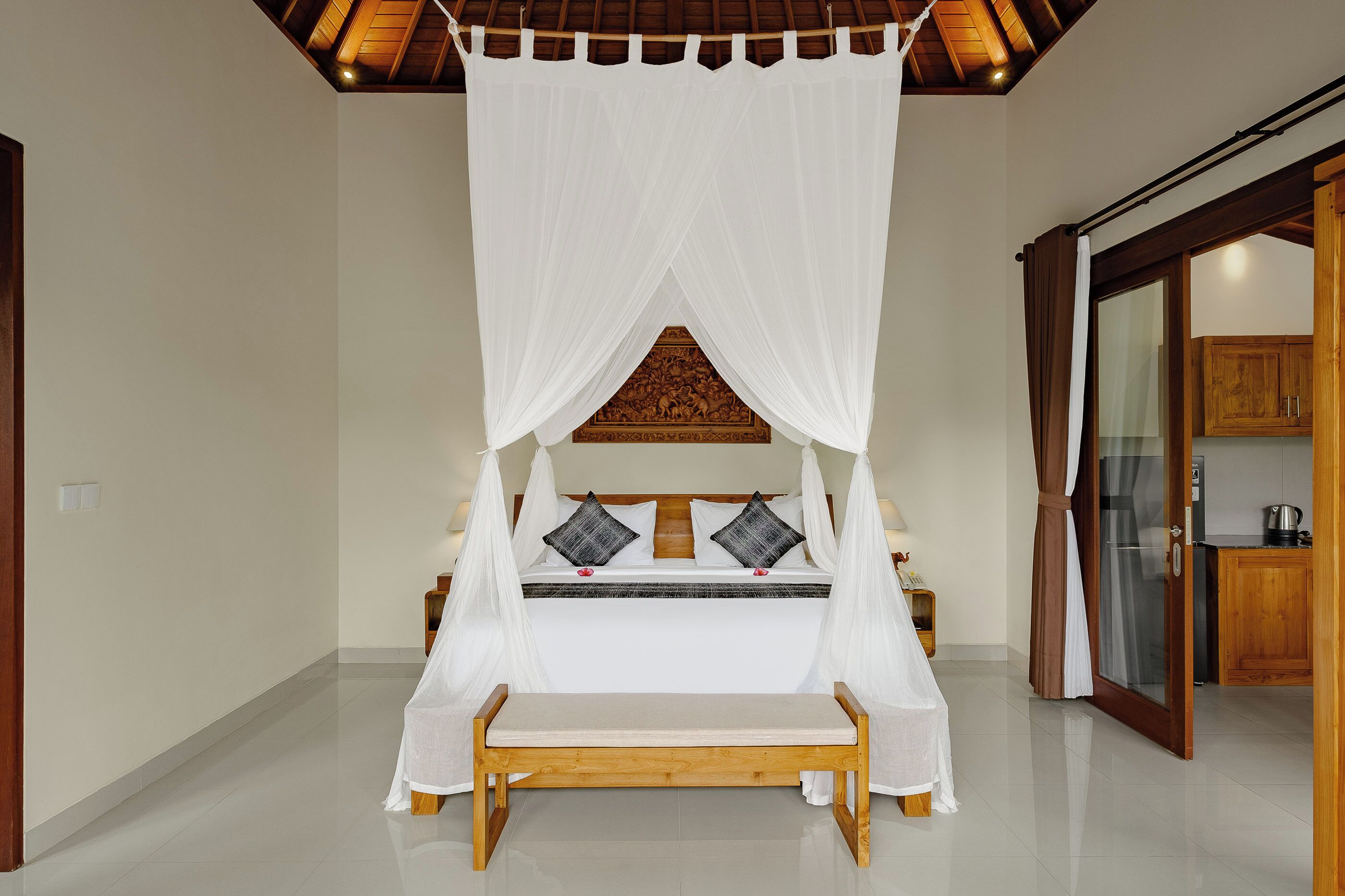 A bedroom with a canopy bed, wooden headboard, and a bench in front.