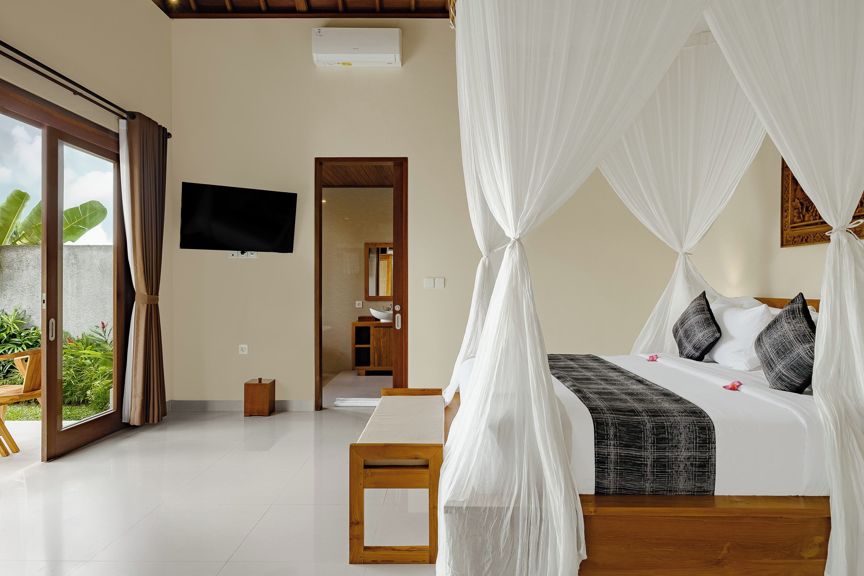 A bedroom with a bed under a canopy, a TV on the wall, and a view of the outdoors.