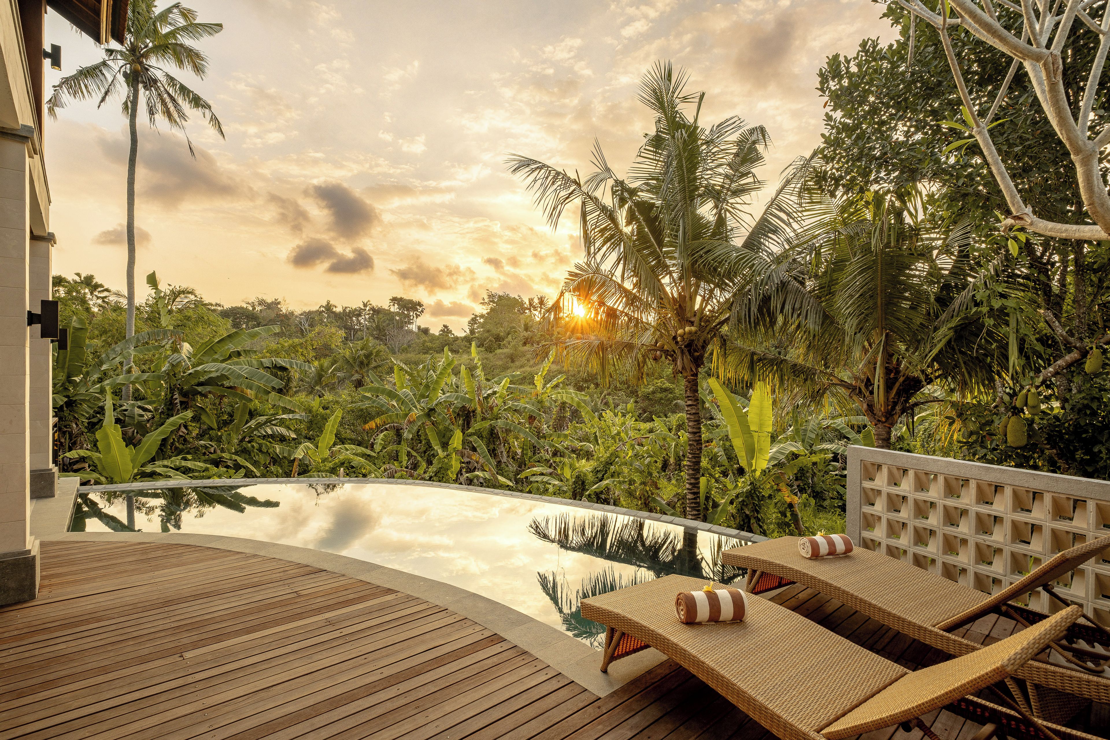 A poolside area with lounge chairs and a view of lush vegetation.