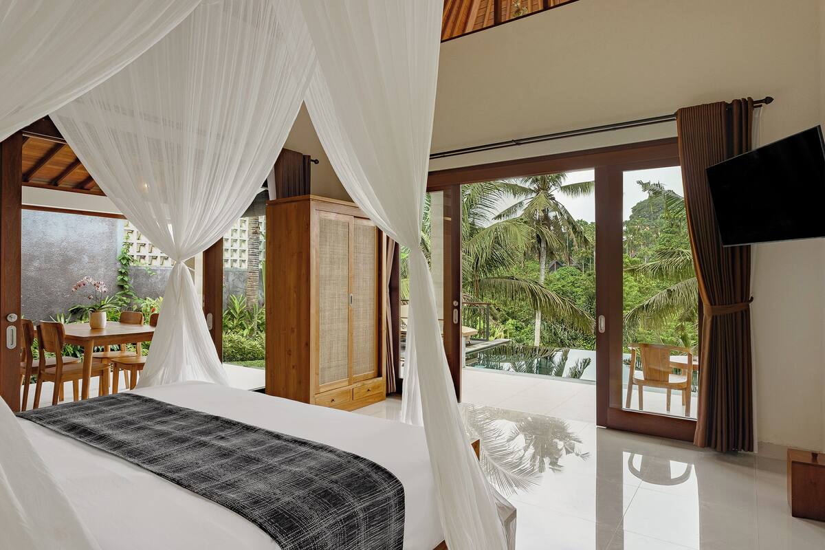 A spacious bedroom with a large bed, a wooden wardrobe, and a TV mounted on the wall.