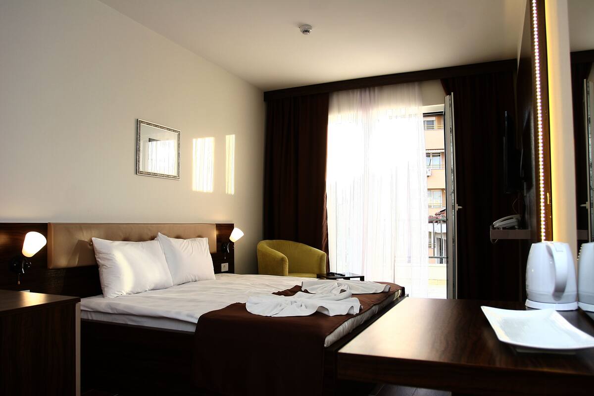 A hotel room with a bed, a desk, a chair, a mirror, and a window with curtains.