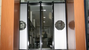 A hotel entrance with a sign reading "Hotel DOA," a crown logo, and two round emblems on the glass doors. - Hotel DOA (Skopje)