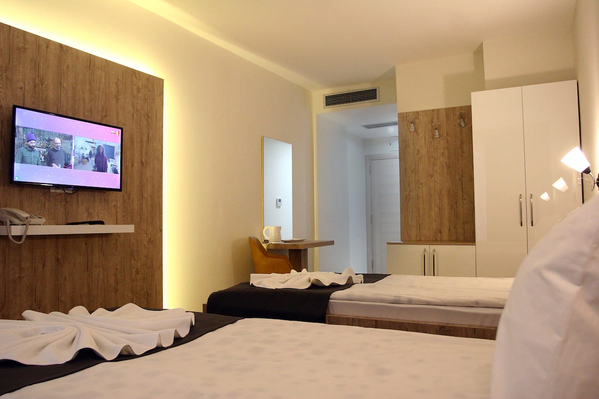 A hotel room with two beds, a television, a mirror, and a wooden wall.