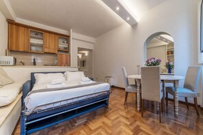 A compact hotel room with a bed, a small kitchenette, a dining area with a table and chairs, and a large mirror reflecting the room. - Lovely one bedroom apartment - Wifi, Independent Heating, A/C, Smart TV (Roma)