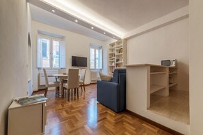 A modern living room with a sofa, a dining table with chairs, a TV, and built-in shelves.