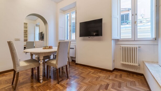 Ein Essbereich mit einem runden Tisch, vier Stühlen, einem an der Wand montierten Fernseher und einem Fenster mit Rollläden.