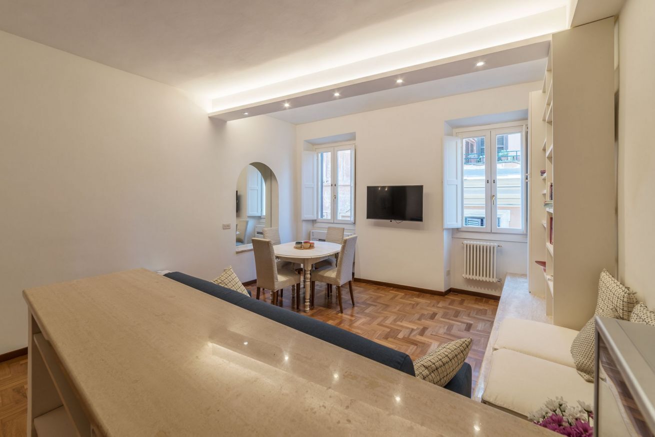 Una sala de estar moderna con comedor, televisor montado en la pared y vista al exterior.