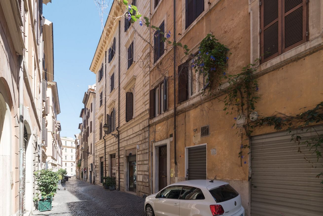 A narrow cobblestone street lined with historic buildings, a parked white car, and a closed shutter on the right.