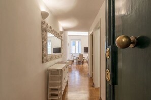 Un couloir avec une commode blanche, un miroir et une porte dotée de poignées en laiton.