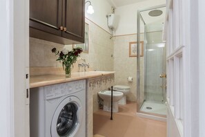 A compact bathroom with a washing machine, toilet, and glass shower enclosure. - Lovely one bedroom apartment - Wifi, Independent Heating, A/C, Smart TV (Roma)