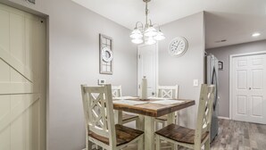 A dining area with a wooden table and white chairs, a chandelier, and a clock on the wall.