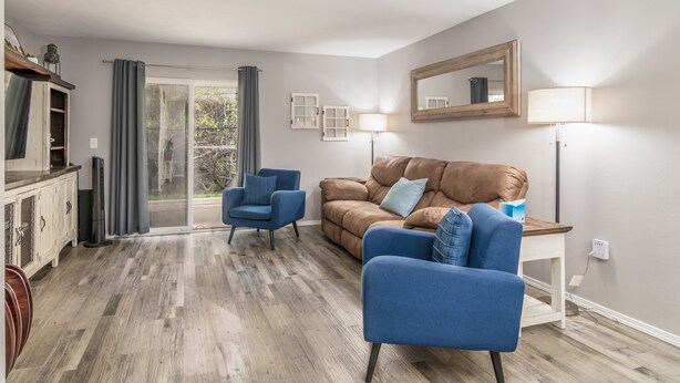 A living room with a brown leather sofa, blue armchairs, a wooden coffee table, and a large mirror on the wall.