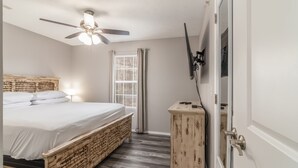 A bedroom with a bed, a ceiling fan, a window with curtains, a bedside table, and a wardrobe.