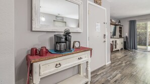 A room with a coffee station, a mirror, a door with a sign, and a view through a glass door.