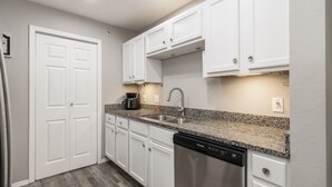 A modern kitchen with white cabinets, a granite countertop, a dishwasher, and a coffee maker.