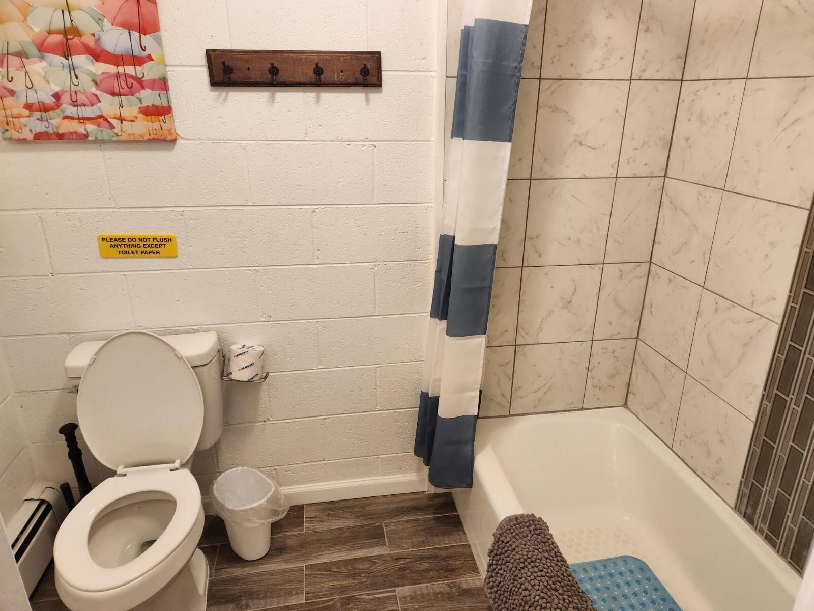 Un baño con inodoro, cortina de ducha, un cartel que indica no tirar nada excepto papel higiénico y un estante de madera sobre el inodoro.