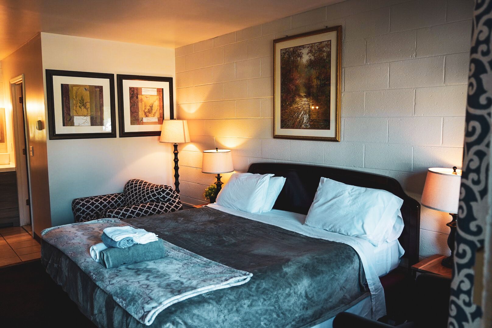 A hotel room with a bed, two bedside lamps, a patterned pillow, a framed picture, and a blanket.