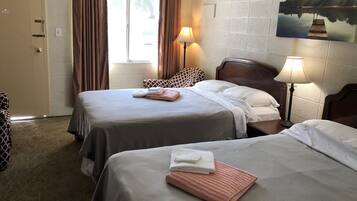 A hotel room with two beds, a window with curtains, a lamp, and a painting on the wall.
