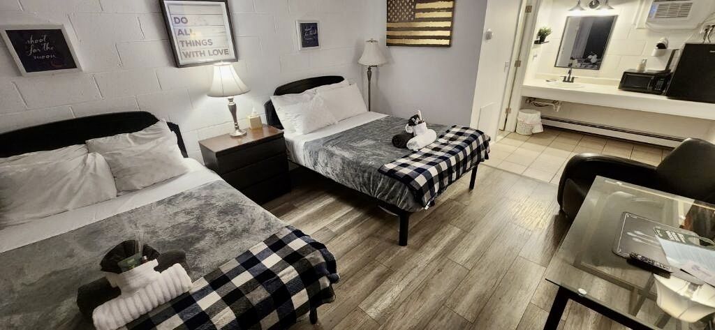 Una camera d'albergo con due letti, una scrivania, una sedia, una TV e un bagno con uno specchio.