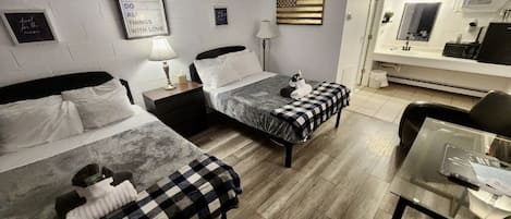 Habitación de hotel con dos camas, un escritorio, una silla, un televisor y un baño con espejo.