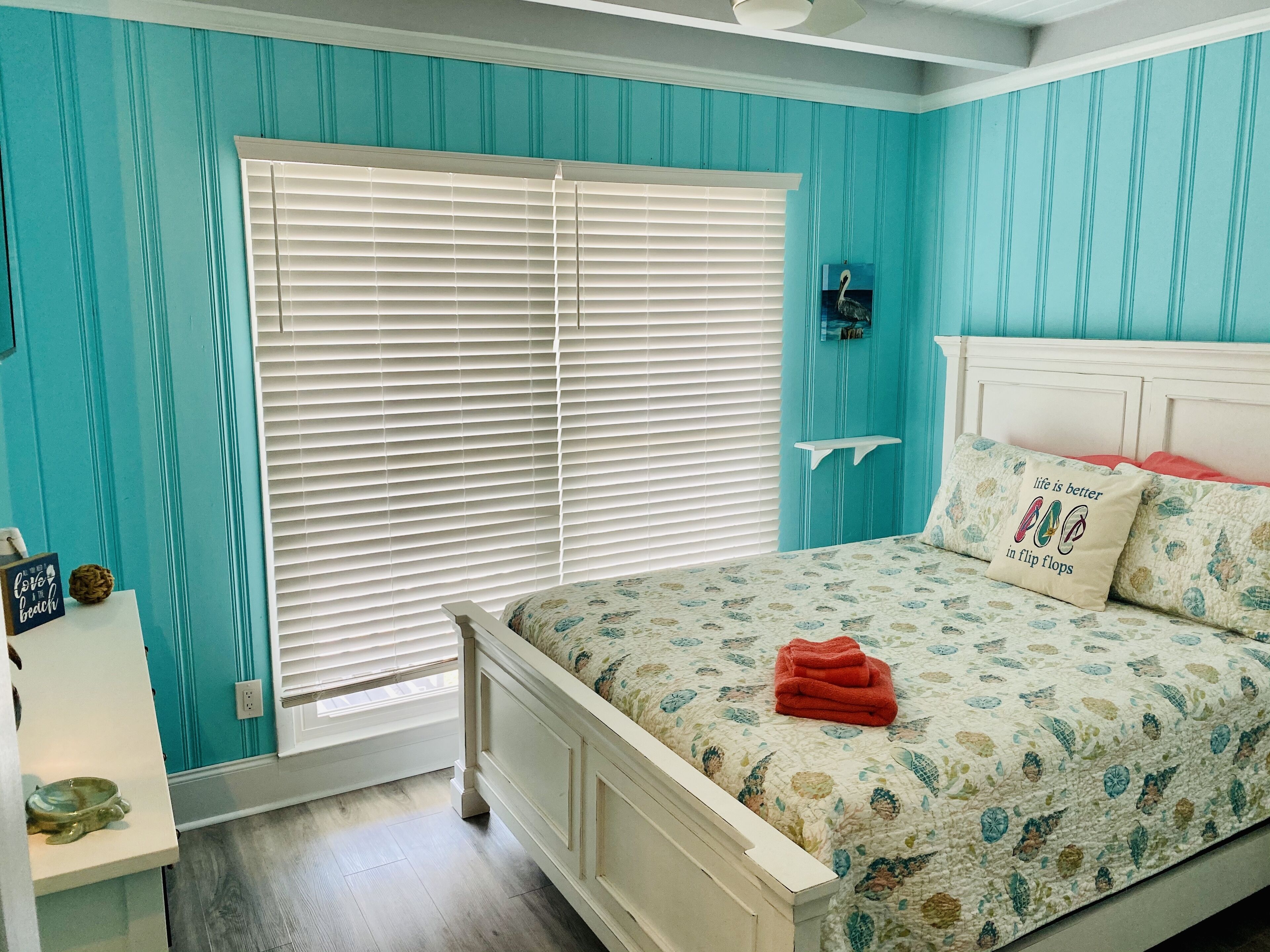 Un dormitorio con paredes color turquesa, una cama blanca y una ventana con persianas.