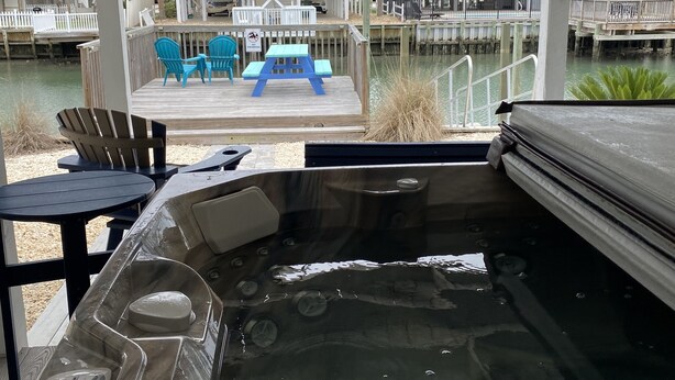 Et område med jacuzzi med udsigt over en ejendom ved vandet, inklusive en badebro og en terrasse med stole og et bord.