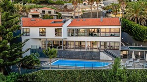 A modern two-story building with a swimming pool, surrounded by lush greenery and other residential buildings. - Vila Crerital - By Wehost (Funchal)