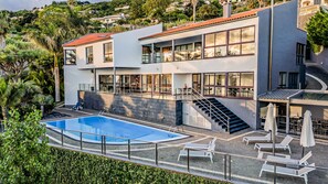 A modern two-story house with a swimming pool, outdoor seating, and a staircase leading to a balcony.