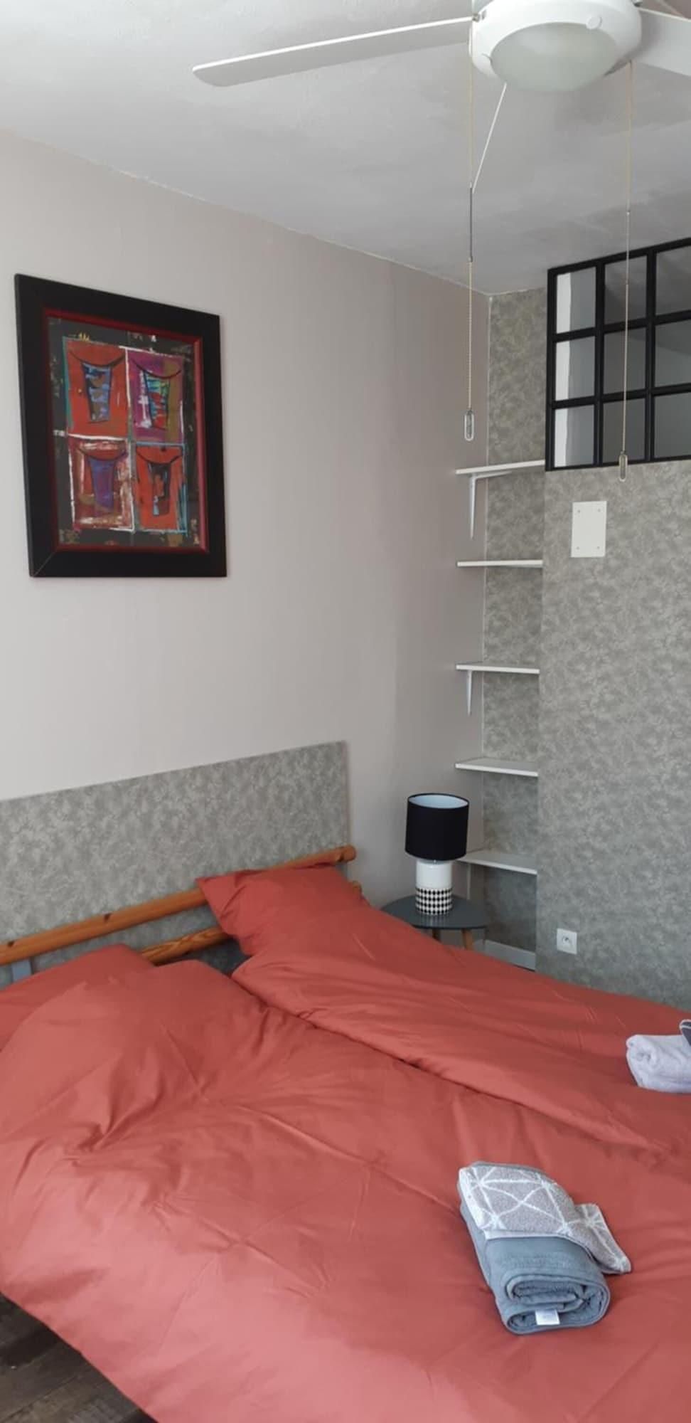 Een slaapkamer met een bed, een plafondventilator, een wandplank en een lijstwerk met kunst.
