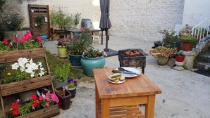 Un patio con mesa de madera, plantas en macetas y una parrilla.