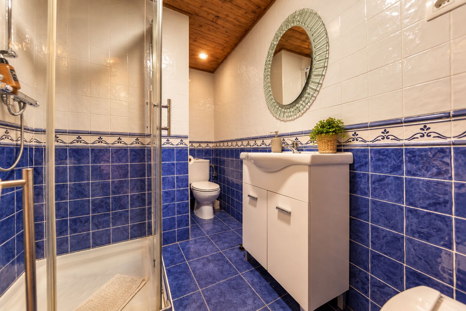 Een badkamer met een douchecabine van glas, een toilet en een wastafel met een decoratieve spiegel erboven.