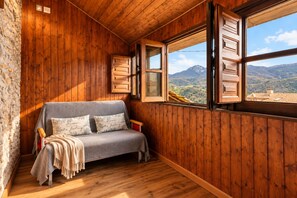 A cozy cabin room with a wooden interior, a bench with cushions, and a large window offering a mountain view. - La Congosta - Jacuzzi, fireplace, and mountains in Asturias (La Villa de Sub, teverga, asturias)