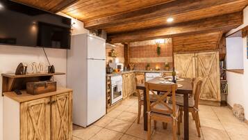A rustic kitchen with wooden cabinets, a dining table with chairs, and a television on the wall.