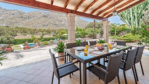 Un patio exterior con una mesa dispuesta para el desayuno, rodeado de sillas, con vistas a montañas y cactus al fondo.