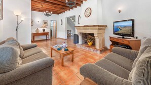 Una sala de estar con chimenea, vigas de madera, un televisor y un comedor con mesa preparada para dos.