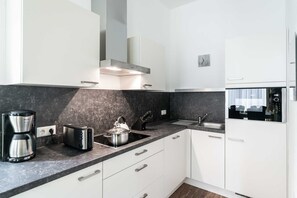 A modern kitchen with white cabinets, a black countertop, a coffee maker, a toaster, and a sink.