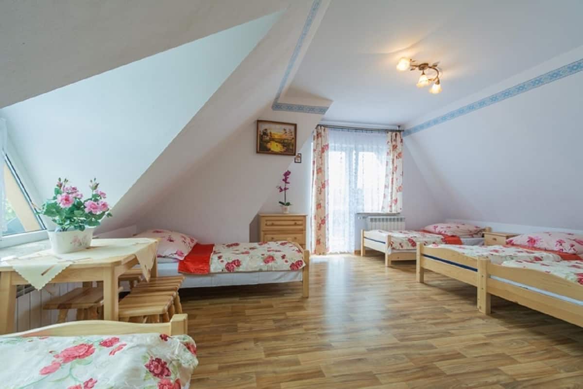 A cozy attic bedroom with wooden floors, two single beds, a small table with a potted plant, and a window with curtains.