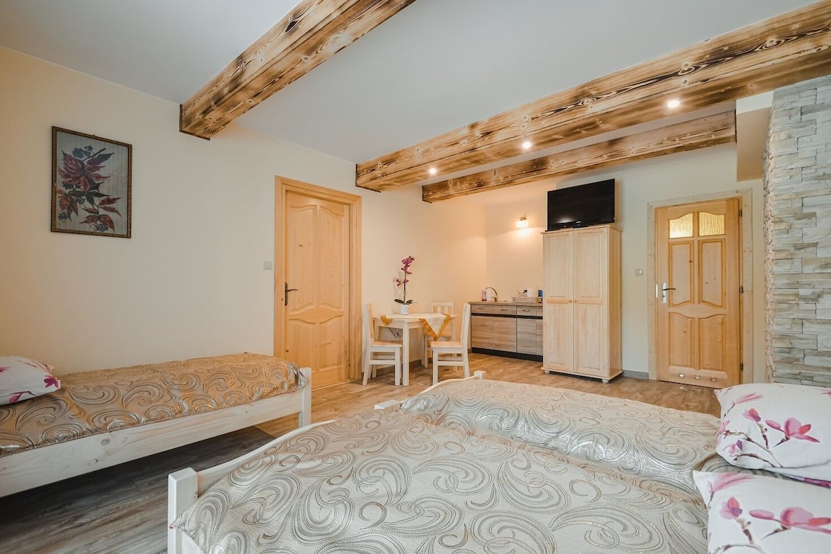 A cozy room with two beds, a wooden ceiling, a dining area, and a kitchen.