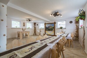 A dining area with wooden tables and chairs, a chandelier, and a scenic painting on the wall.