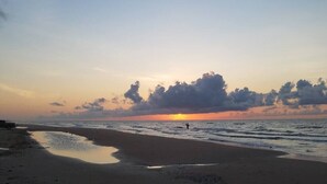 Una playa al atardecer con un mar tranquilo y una persona caminando por la orilla.