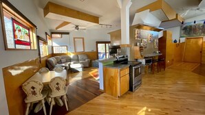 A spacious living area with a sofa, dining table, and chairs, a kitchen with a stove and microwave, and a large window providing natural light. - One of a kind cabin in the woods.  Quiet and private but close to everything.  (Coxs Creek)