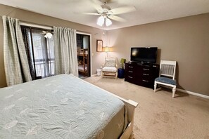 Un dormitorio con una cama, televisor, cómoda, silla y ventilador de techo.