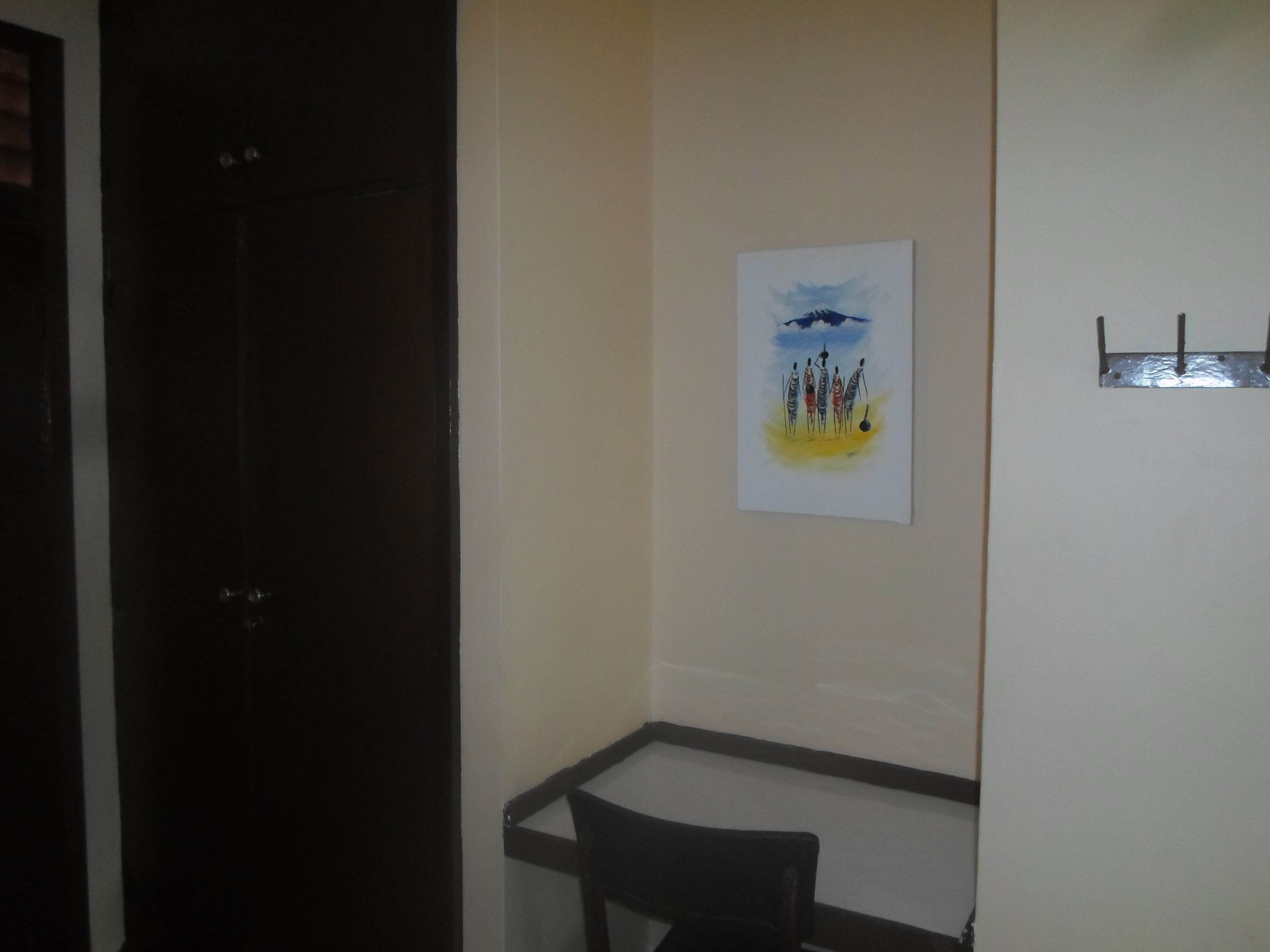 A hallway with a door on the left, a chair in the center, and a painting on the wall.